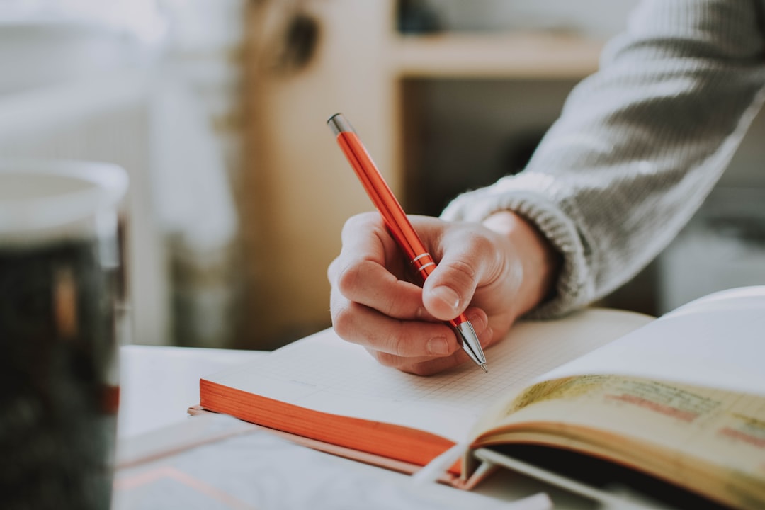 Hand holding a red pen while writing notes on a book, representing practicing skills independently without AI