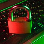 Red padlock resting on a black computer keyboard, representing password and account security